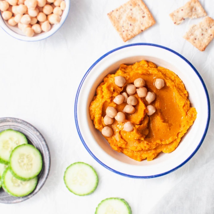 bowl of pumpkin hummus topped with chickpeas served with cucumber slices and crackers