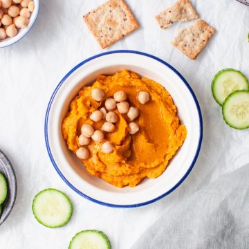 bowl of healthy pumpkin hummus topped with chickpeas served with cucumber slices and pitta crisps
