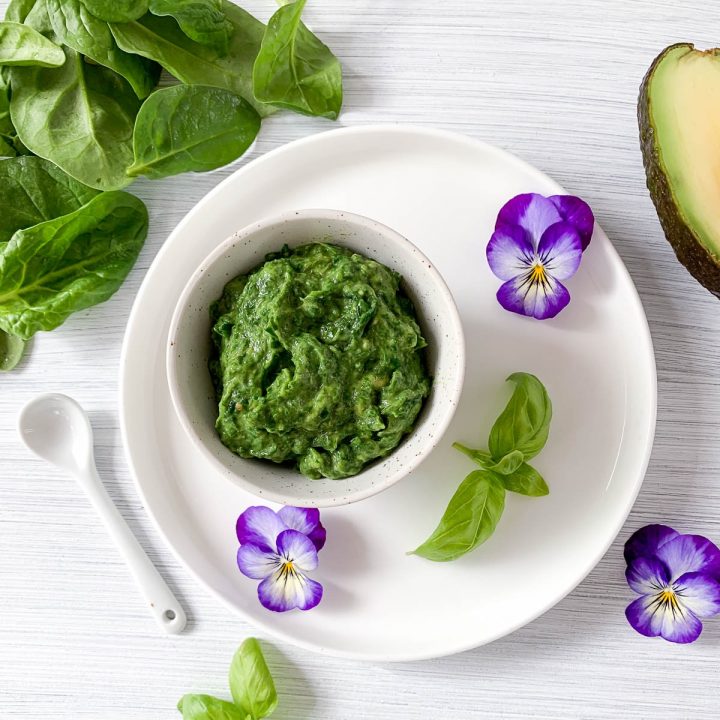 white bowl of avocado spinach pesto decorated with purple edible flowers
