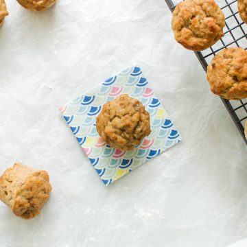 mini banana muffins on cooling rack, one in the centre on blue and yellow patterned paper