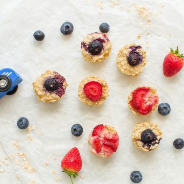 blw snack porridge bites on white background scattered with blueberries, strawberries and oats
