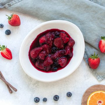 mixed berry compote in white bowl surrounded by strawberries and blueberries