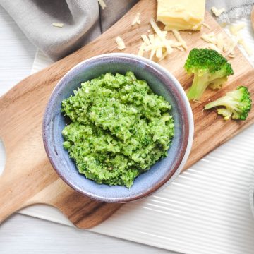 blue bowl filled with broccoli spinach pesto with leftover broccoli florets and cheddar cheese