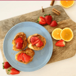 blue plate on wooden board with three slices or torrijas topped with strawberries