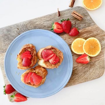 three pieces of torrijas on a blue plate topped with fresh strawberries