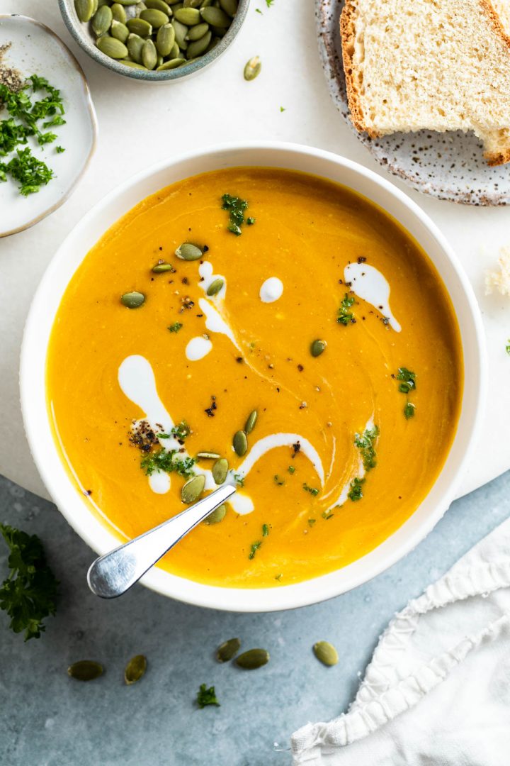 bowl of creamy carrot soup with a spoon in it ready to eat, slices of bread just visible