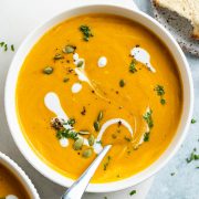 bowl of pumpkin carrot soup drizzled with coconut milk and topped with pumpkin seeds and parsley with a spoon in it ready to eat