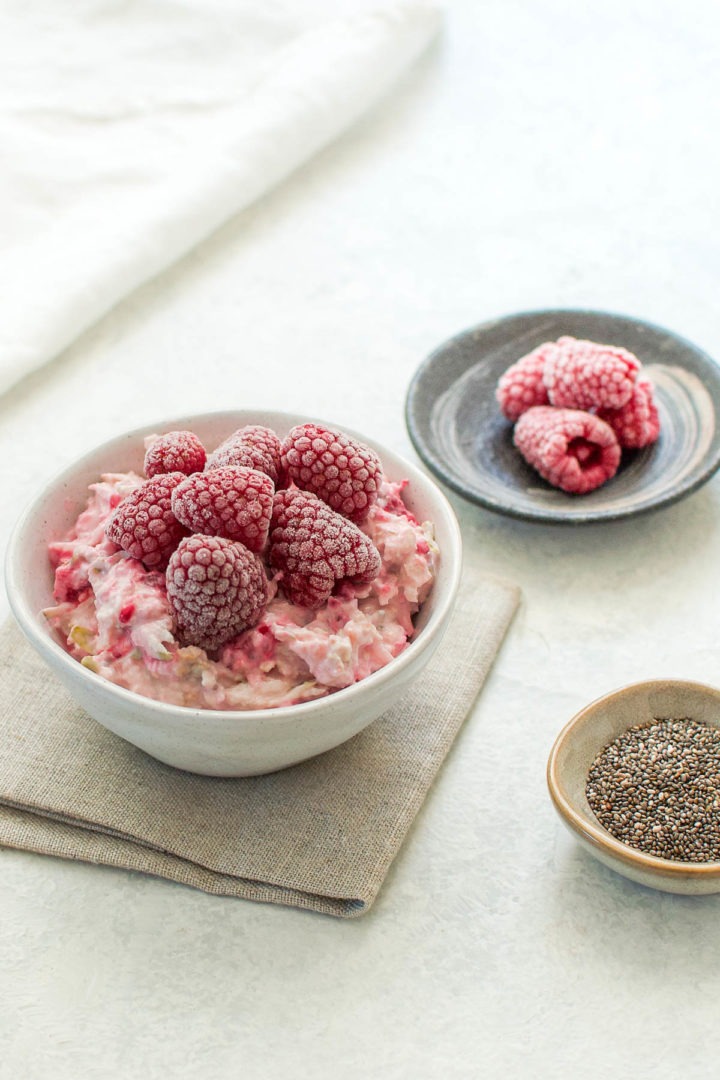 45 degree angle shot of raspberry bircher muesli with frozen raspberries blurred out int eh background