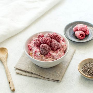 raspberry bircher overnight oats topped with frozen raspberries