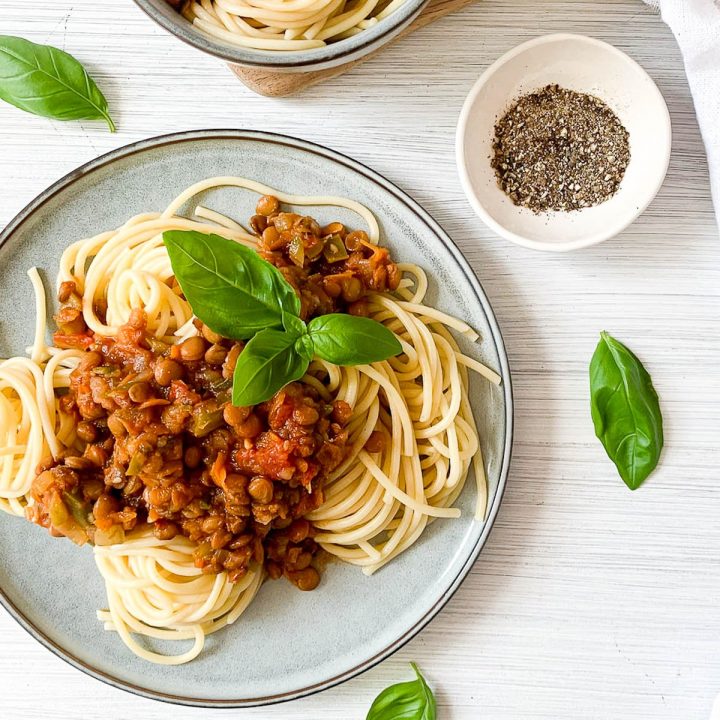 lentil bolognese on spaghetti in blue plate topped with fresh basil