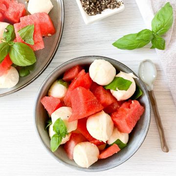 blue bowl of watermelon and mozzarella salad topped with fresh basil leaves and blue spoon to the right