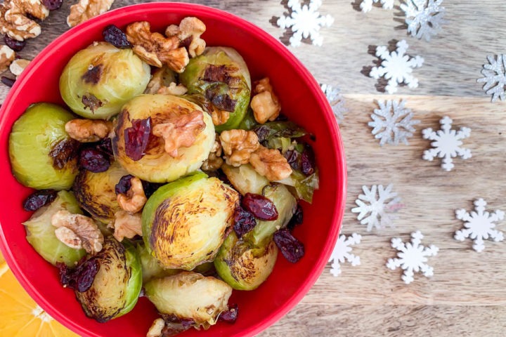 red bowl filled with brussels sprouts, walnuts and cranberries with white snowflakes to the right