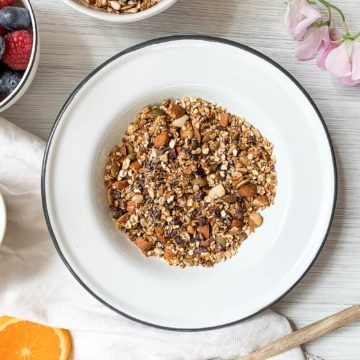 healthy no added sugar granola in white bowl served with berries and yogurt to the left hand side