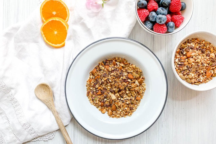 white bowl filled with granola with berries above it and orange slices