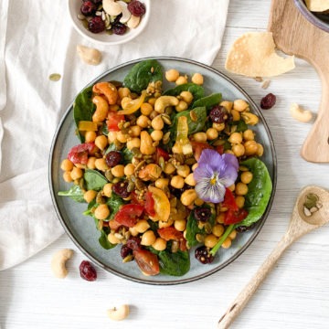 plant based chickpea salad on blue plate with nuts, spices and dried fruit, served with mini poppadoms
