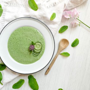 cucumber soup in white bowl decorated with cucumber slices and a purple chive flower
