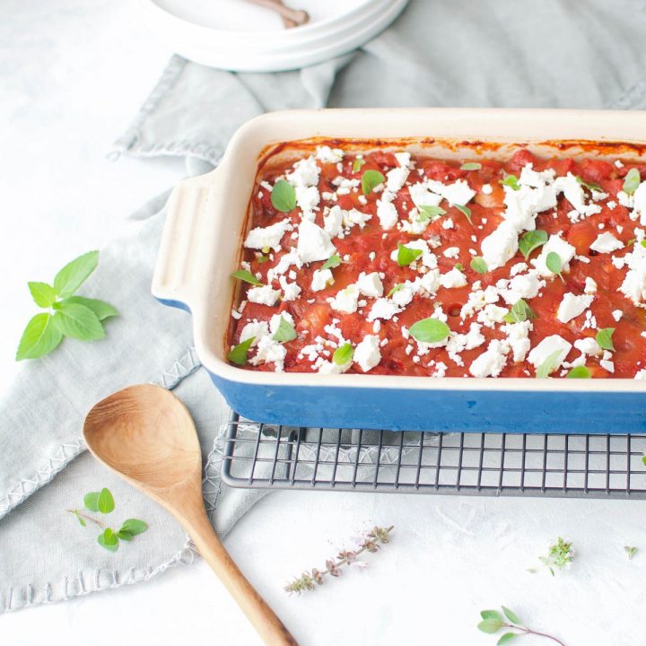 blue baking dish of gigantes plaki topped with feta cheese and fresh herbs