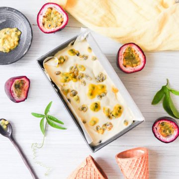 rectangle tin of passionfruit ice cream surrounded by passionfruit leaves, passionfruit halves and ice cream cones