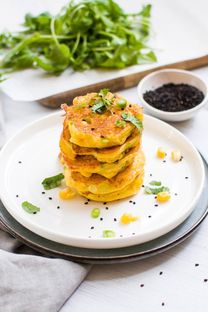 close up of stack of corn fritters sprinkled with black sesame seeds and chopped spring onions