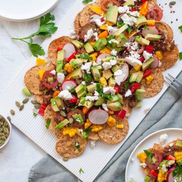 vegetarian nachos on white serving platter with pumpkin seeds scattered over the nachos and table