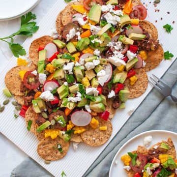 quick and easy vegetarian nachos on white platter with pumpkin seeds to sprinkle over