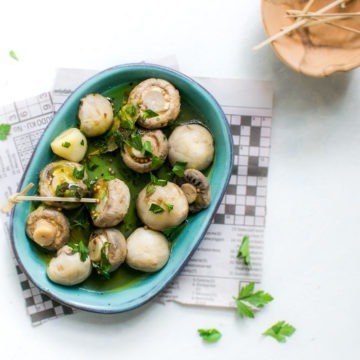 blue plate of marinated mushrooms sprinkled with fresh parsley and served with toothpicks to eat