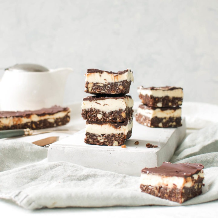 Three Nanaimo bars stacked on top of each other with a teapot in the background