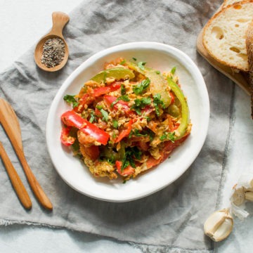 white bowl of eggs piperade on dark cloth with slices of bread to serve