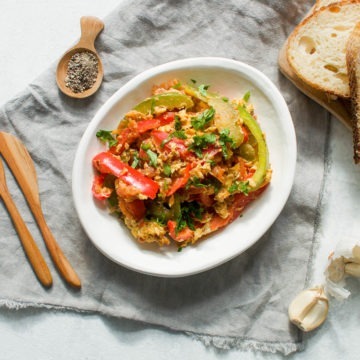 eggs piperade scrambled eggs with red and green bell peppers in white dish served with slices of bread