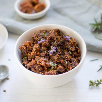 angled view of black olive tapenade with fresh rosemary sprigs, dried figs and olives in the background