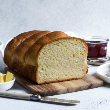 cut milk bread to see the fluffy interior of the loaf. A pot of jam in the background