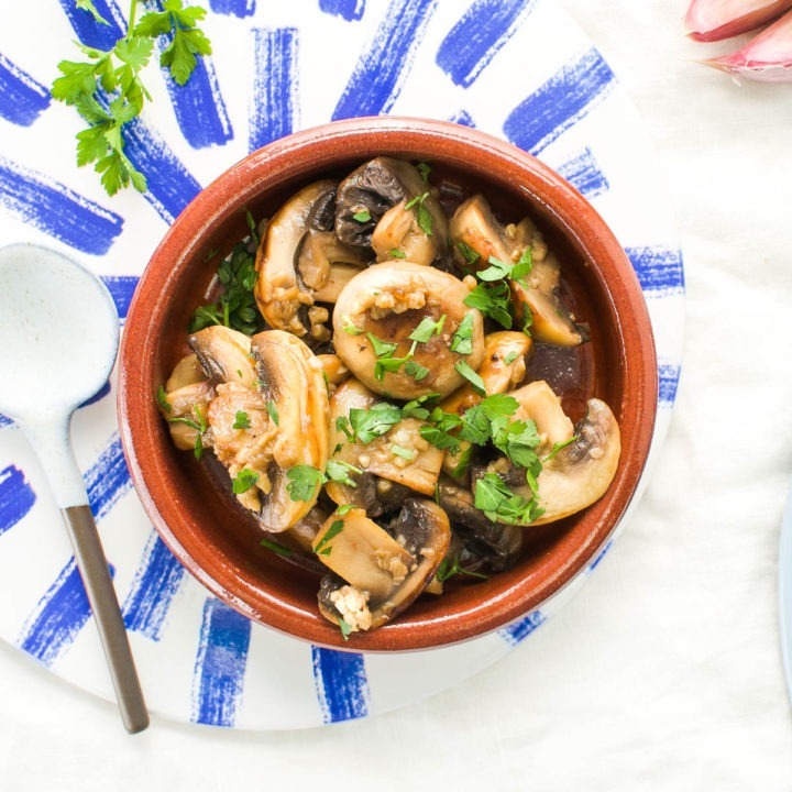 overhead image of ajillo mushrooms in Spanish terracotta dish, sprinkled with fresh parsley