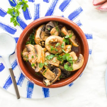 overhead image of mushroom tapas in terracotta dish on blue tile with bread to the side, ready to mop up the last fo the garlic olive oil