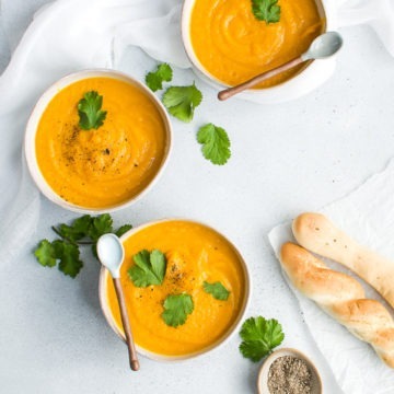 Three bowls of carrot and coriander soup with bread sticks