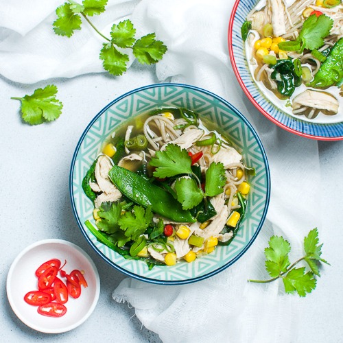 Bowl of chicken noodle soup with side dish of chillies