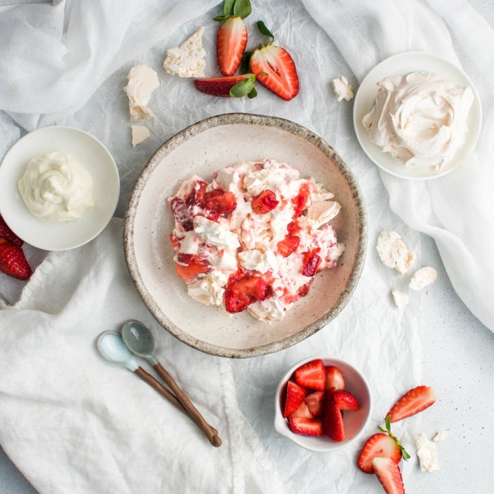 eton mess in a bowl with fresh strawberries, meringue and cream around the bowl