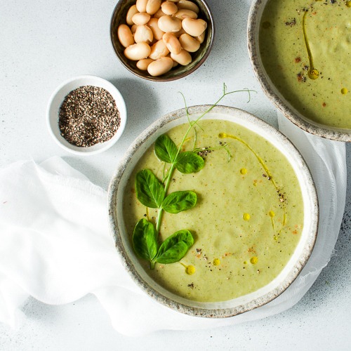 Bowl of green soup with small bowl of pepper and beans