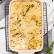 baking dish with mac n cheese with a portion taken out to show the creamy pasta filling. Decorated with fresh thyme.