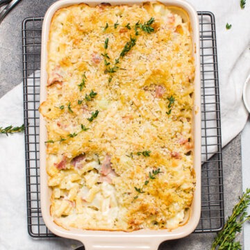 baking dish with mac n cheese with a portion taken out to show the creamy pasta filling. Decorated with fresh thyme.