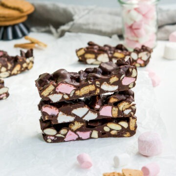 stack of three pieces of rocky road on white background with marshmallows and digestive biscuits around