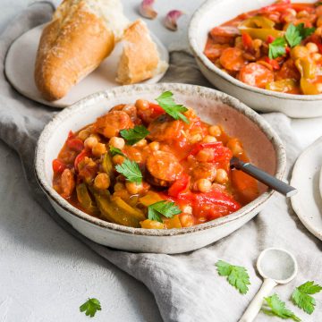 Spanish chickpea and chorizo stew sprinkled with parsley with fresh bread in the background