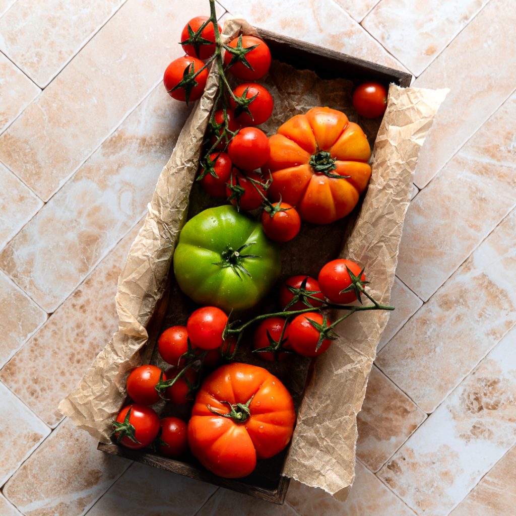A rectangular wooden tray filled with different varieties of tomatoes.