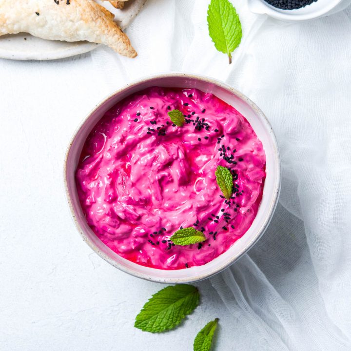 bright pink beetroot raita in a pale bowl decorated with fresh mint leaves and nigella seeds