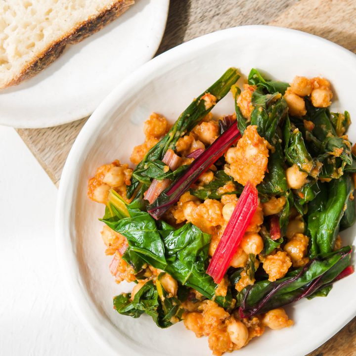 a white plate of silverbeet and chickpeas on a wooden board, the pink, yellow and red stems of the chard visible to show they are used in the dish