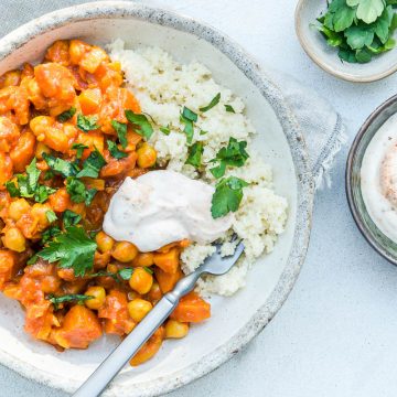 overhead view of one bowl of chickpea tagine with couscous, yogyrt and fresh parsley, a bowl of extra harissa yogurt to its right