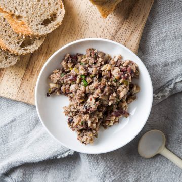 mushroom tapenade in white bowl on wooden chopping board next to slices of baguette, ready to serve
