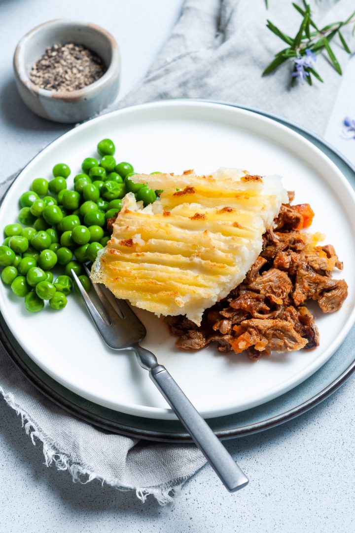Close up of leftover lamb shepherds pie serving on a plate with peas.