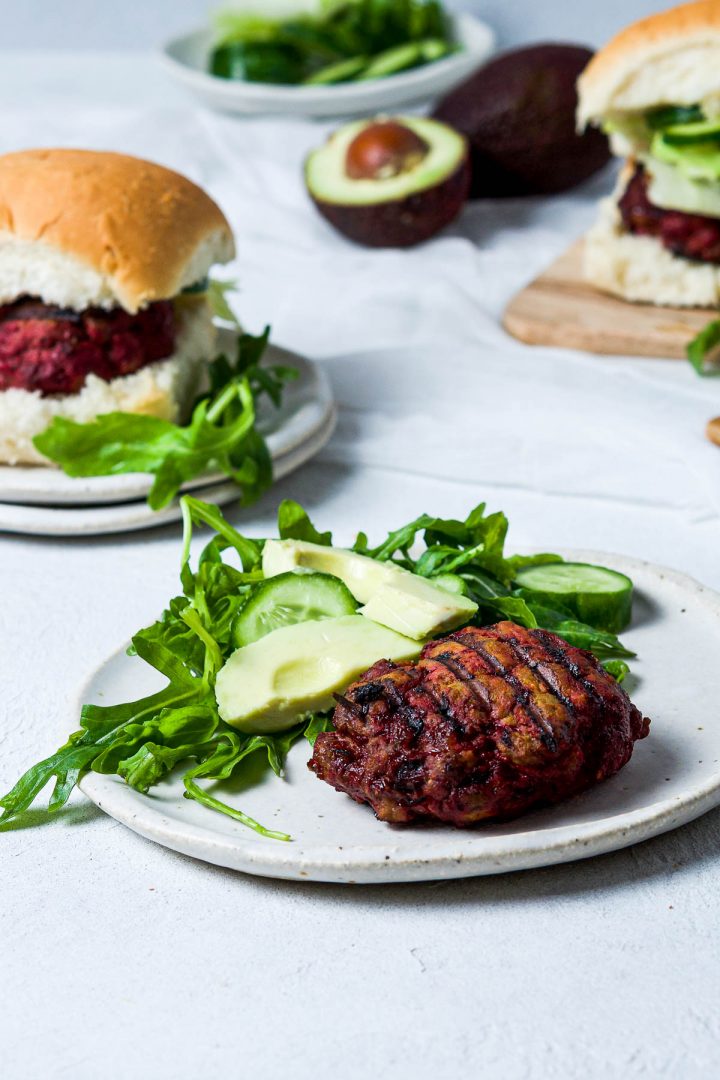 beetroot burger on a plate with avocado, cucumber and rocket salad