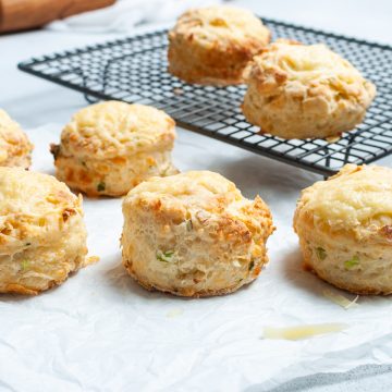 freshly baked cheese and onion scones, some cooling on a wire rack, others on baking paper