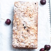 overhead shot of cherry bakewell cake dusted with icing sugar, with fresh cherries dotted around